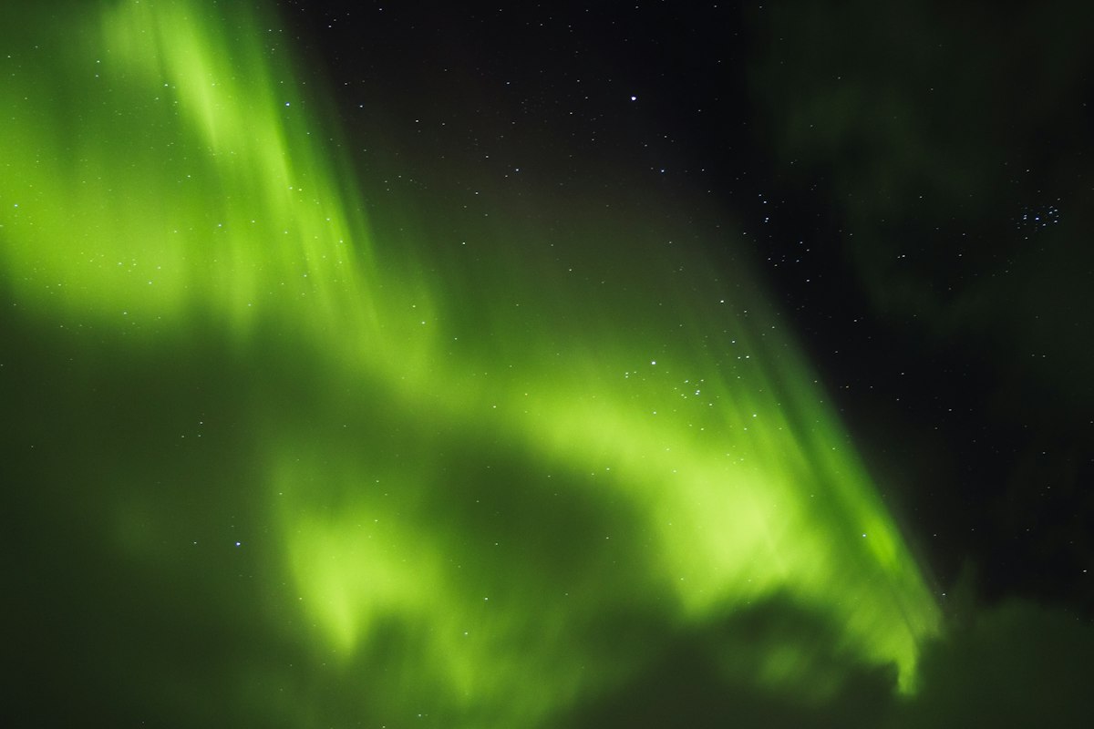 A bright green aurora with long vertical rays fills the night sky over Iceland, with stars showing through the thinner parts of the display.