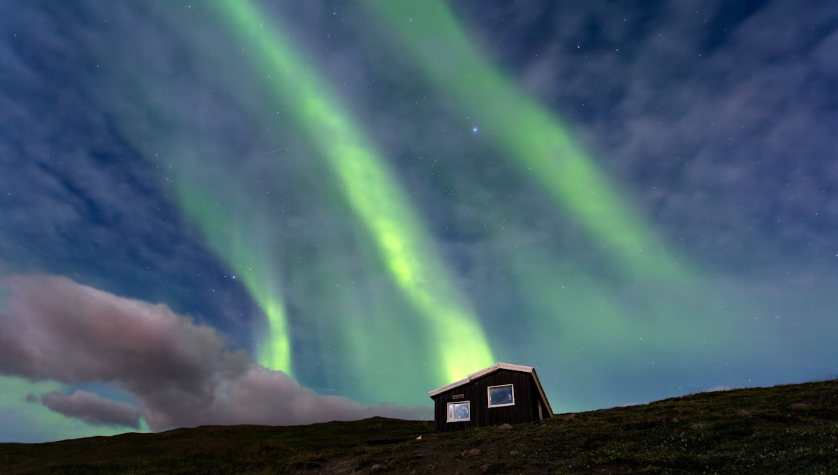 A house on a hillside beneath a green aurora arc on a clear winter night above Akureyri in North Iceland.