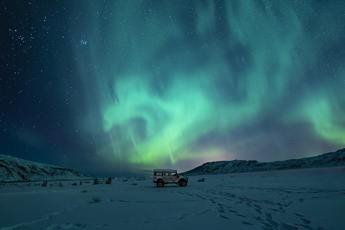 A black SUV parked on a snow-covered field under a green aurora, the kind of winter night drive a January aurora trip in Iceland depends on.