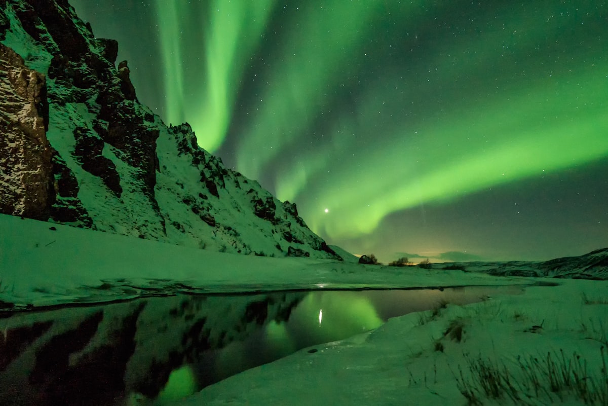 Green aurora rippling above a snow-covered mountain under a dark, star-filled Iceland sky — the deep, long nights that November brings to the aurora calendar.