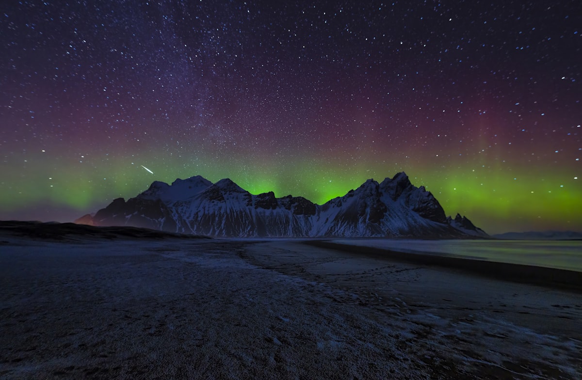 Green aurora arc above the snow-dusted peaks of Vestrahorn in southeast Iceland, framed by a starry sky — the kind of clear autumn night September brings back to the calendar.