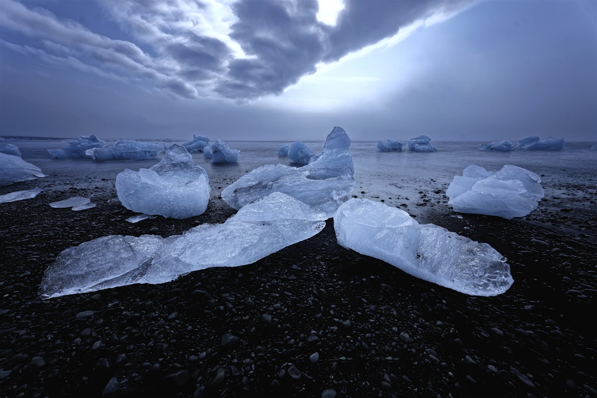 Glacial icebergs glistening on the black volcanic sand of Diamond Beach in southeast Iceland under a dark sky.