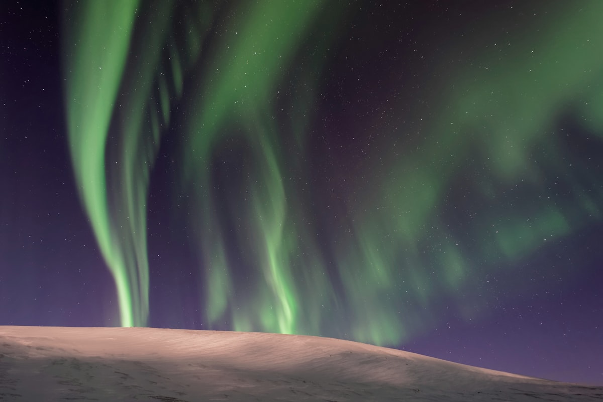Green aurora arcs over a snow-covered landscape in North Iceland on a clear, dark winter night.