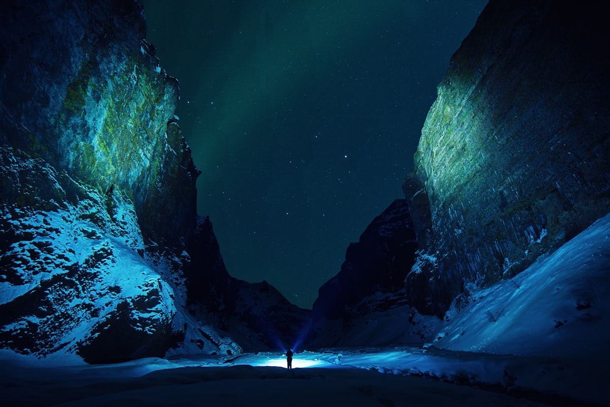 Green aurora borealis arcing over a dark Icelandic canyon at night, the kind of remote dark-sky location a self-drive aurora hunter can reach.