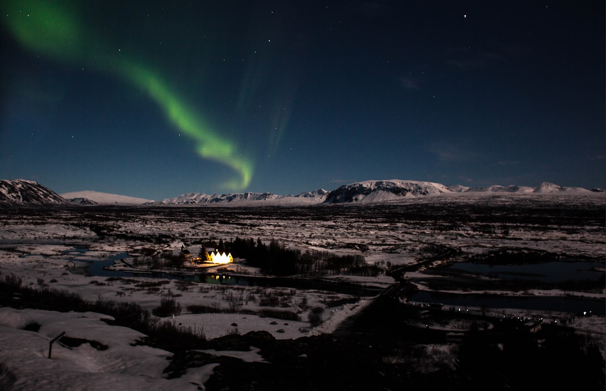 Aurora borealis arcing across the night sky over Þingvellir National Park in Iceland, with the rift valley landscape below.