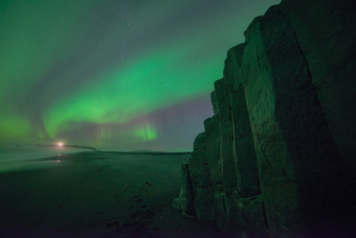 The northern lights arcing in green bands over the dark rocky coastline near Vík in South Iceland.
