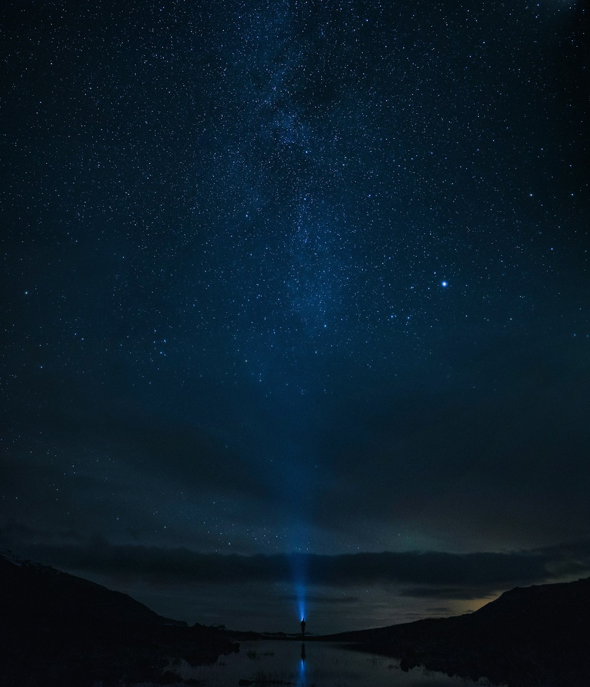 A person stands beneath a faint band of northern lights and a star-filled sky in Iceland, close to how the aurora appears to the naked eye on an average night.