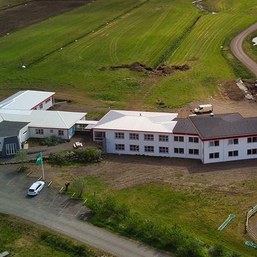 Aerial view of the Brunnhóll farm complex set among green fields beneath the glacier