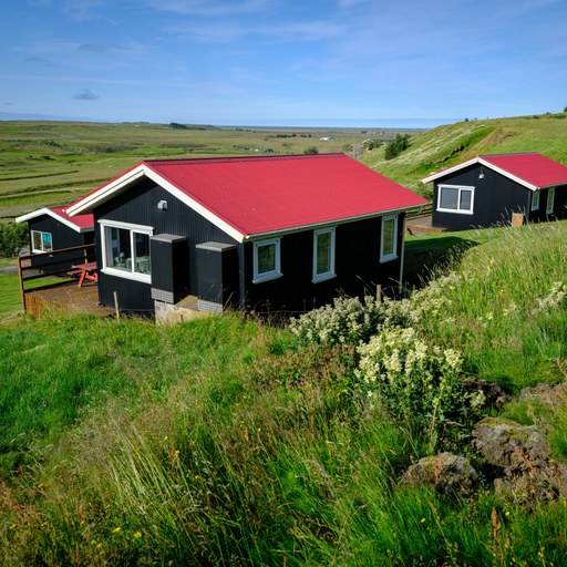 Two black cottages with red roofs at Hestheimar, on a green slope above the South Iceland plains