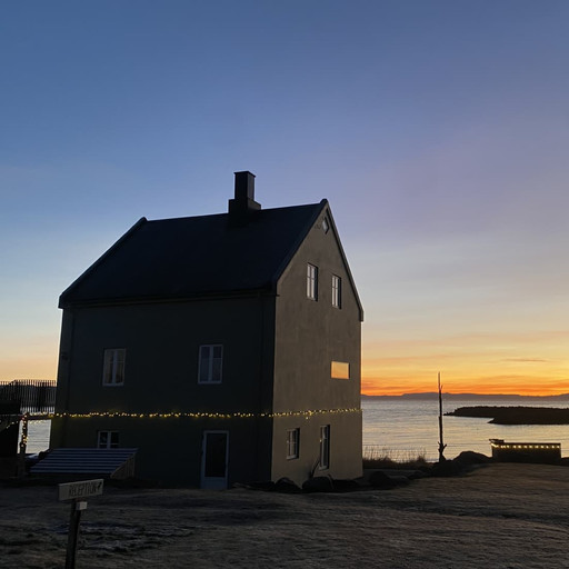 Melar Guesthouse silhouetted against a sunset over the sea at Kópasker