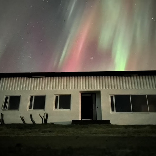 The northern lights over the farmhouse at Óspaksstaðir, green and red curtains filling the sky above the roof