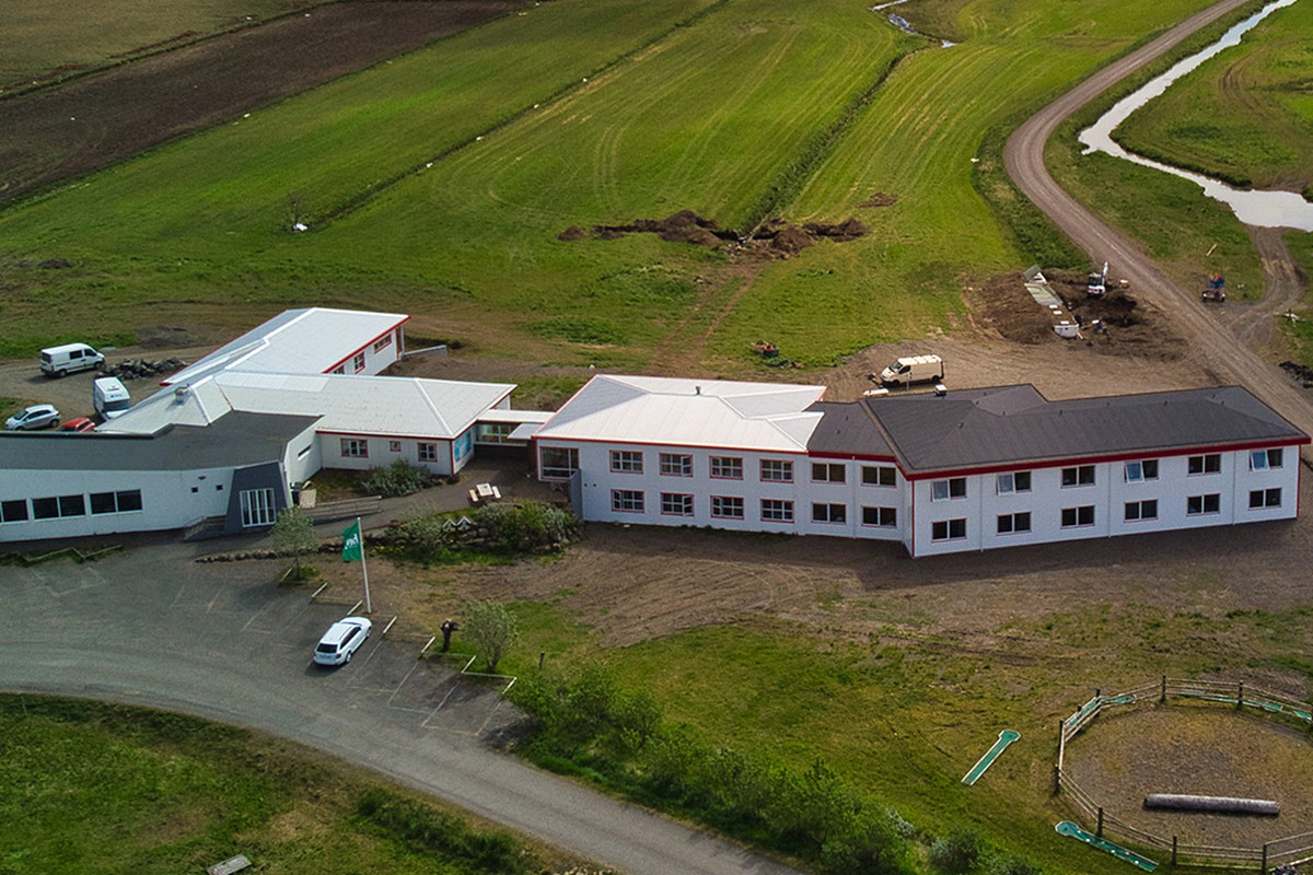 Aerial view of the Brunnhóll farm buildings among green fields beneath Vatnajökull