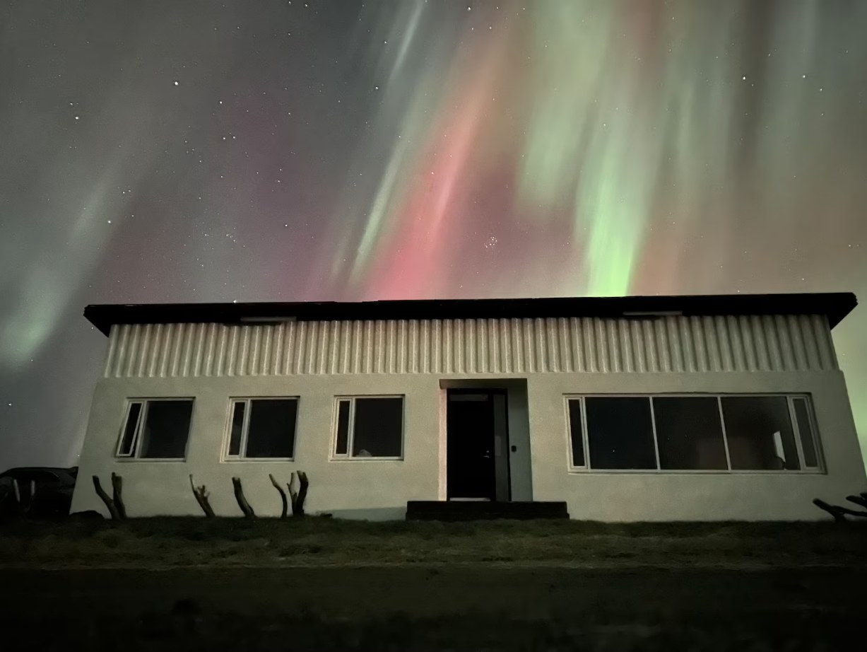 The northern lights over the farmhouse at Óspaksstaðir, green and red curtains of aurora filling the night sky above the roof