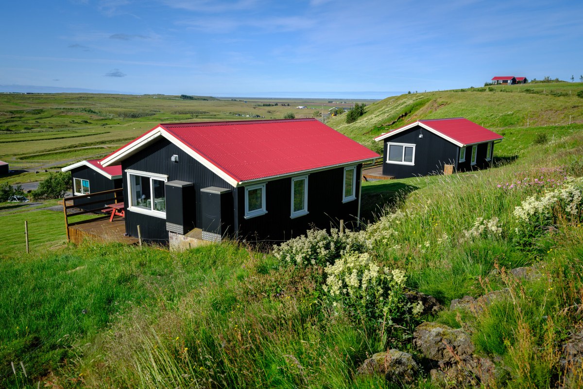 Two black cottages with red roofs at Hestheimar, on a green slope above the South Iceland plains