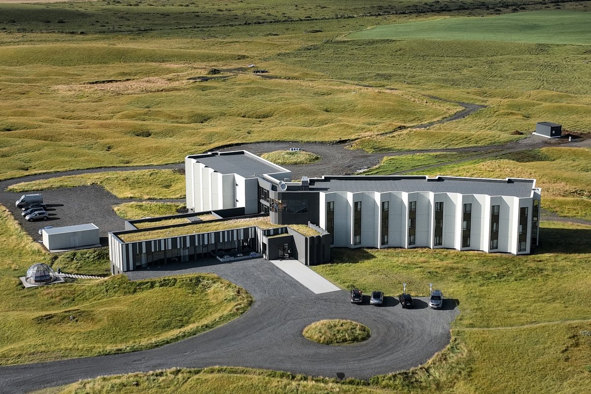 Landhotel seen from the air, a long low building with a grass roof standing alone in open farmland