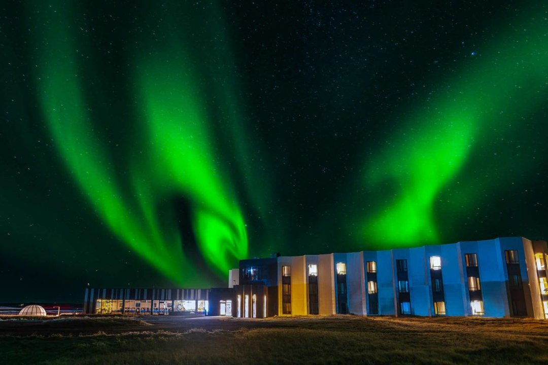 Green aurora filling the sky above the full length of the lit Landhotel building