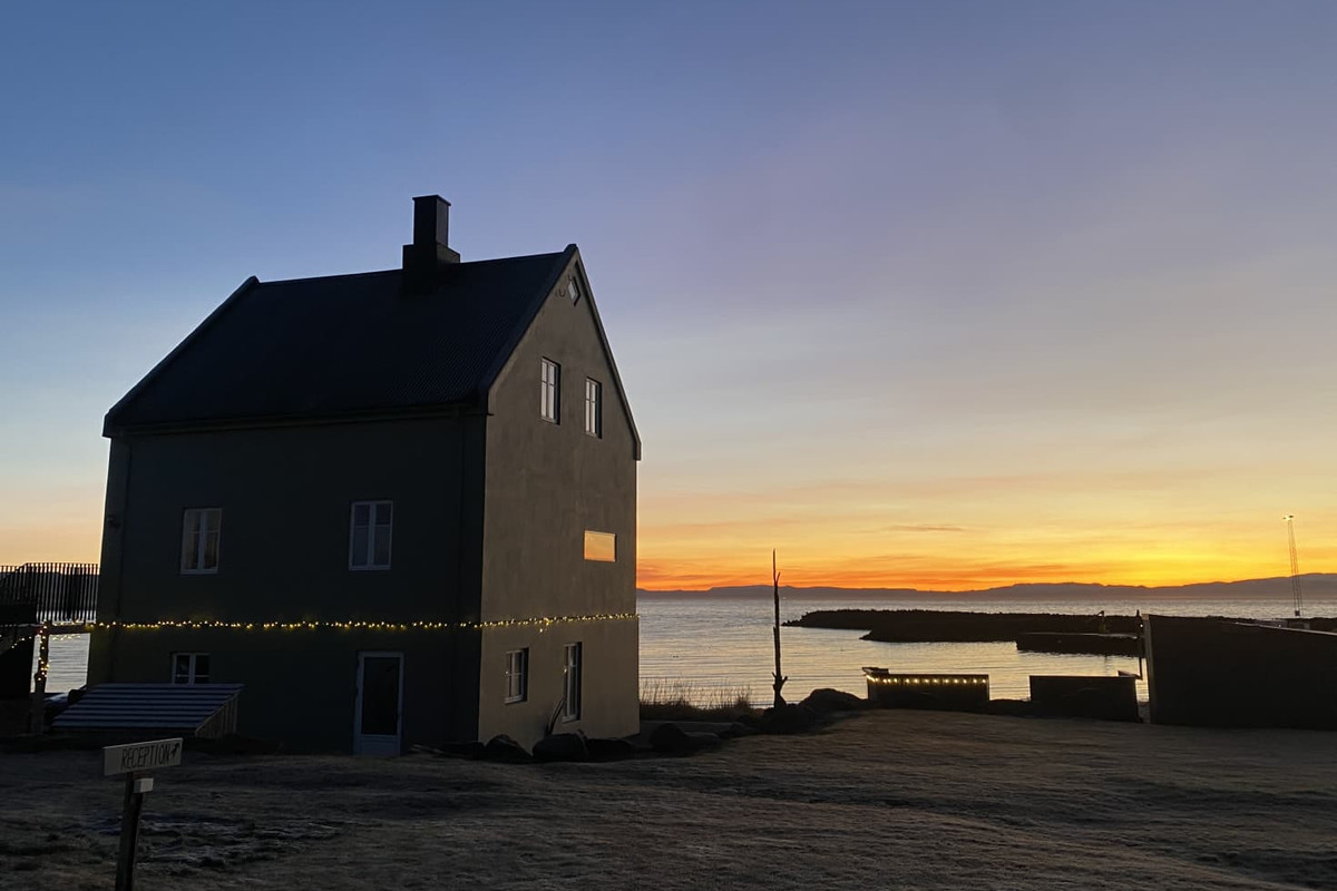 Melar Guesthouse silhouetted against a sunset over the sea at Kópasker